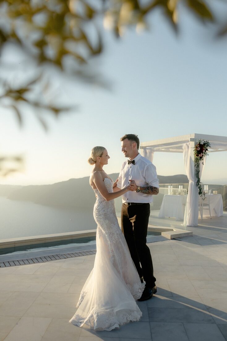 Couple dancing on a terrace at sunset, with a wedding arch and the sea behind them