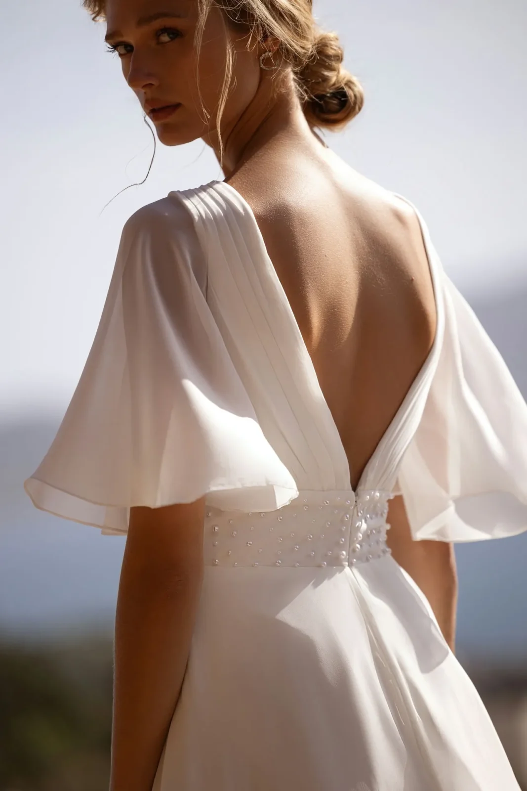 a model wearing a greek goddess wedding dress in white with an open back by designer demetrios