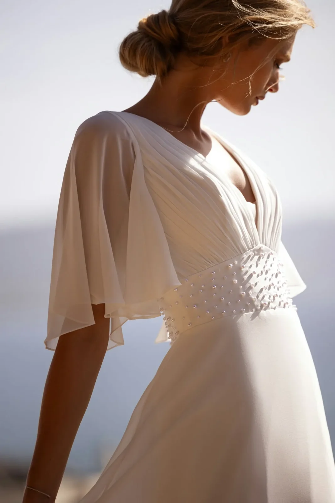 a model wearing a greek goddess wedding dress in white with elegant draping by designer demetrios