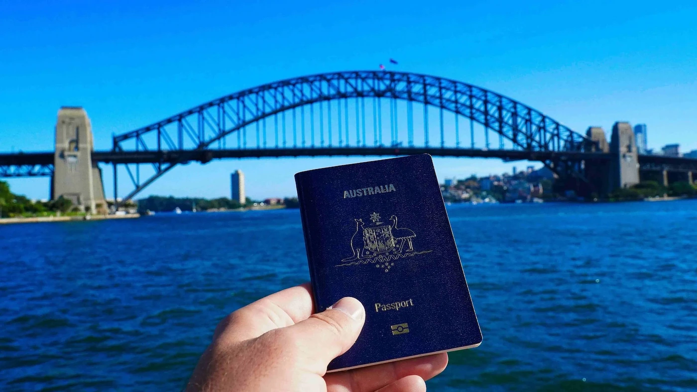 a man holding an australian passport with a bridge behind