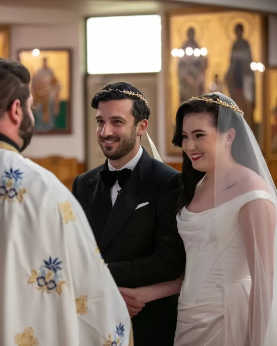greek orthodox wedding with bride and groom wearing gold stefana standing at the altar in front of the priest