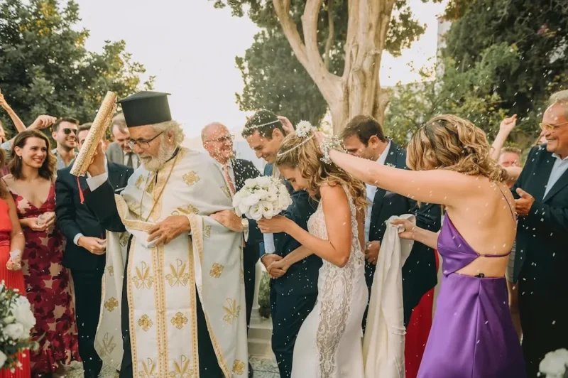 A Greek Orthodox priest leading a bride and groom in their wedding crowns through the dance of Isaiah as guests throw rice