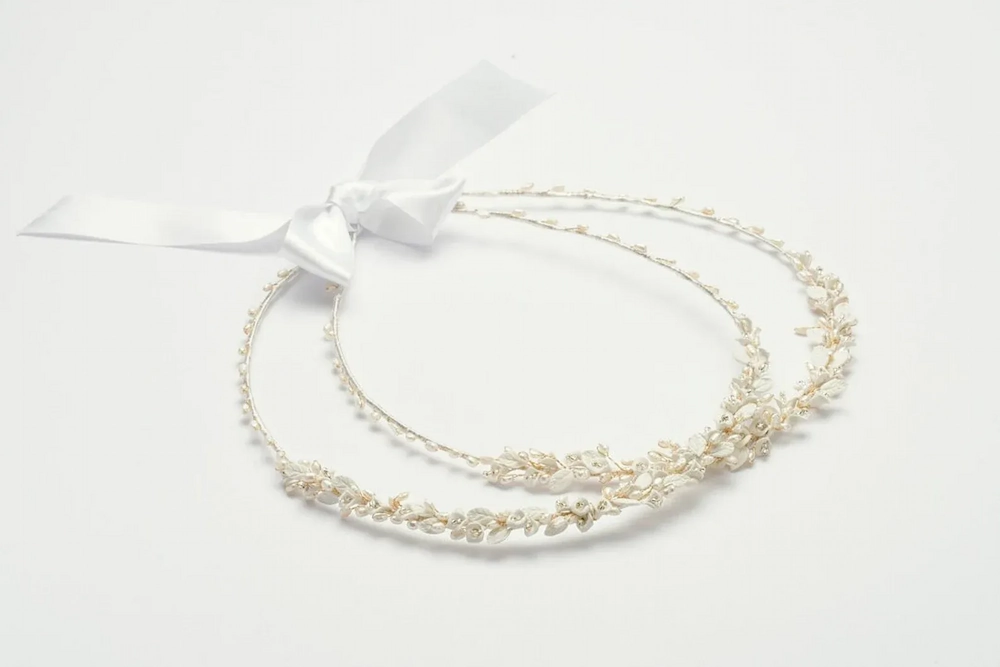 A pair of Greek wedding stefana joined by a white satin ribbon, laid flat on a white background