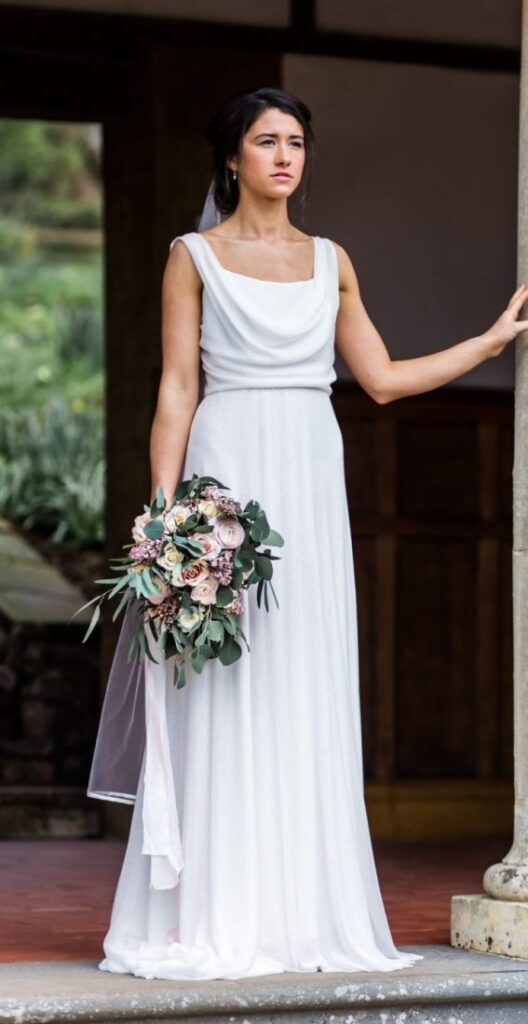a bride in white wearing a greek goddess aphrodite style wedding dress holding flowers