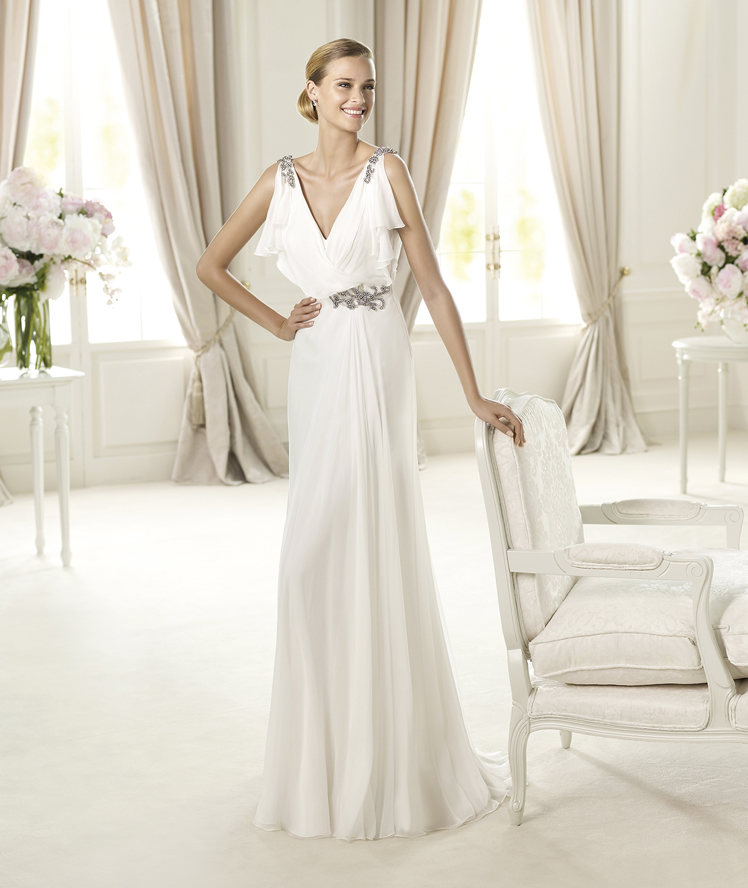 a bride in white wearing a greek goddess wedding dress leaning on a chair
