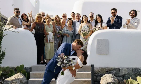 groom kisses bride while guests look on at kalesma mykonos