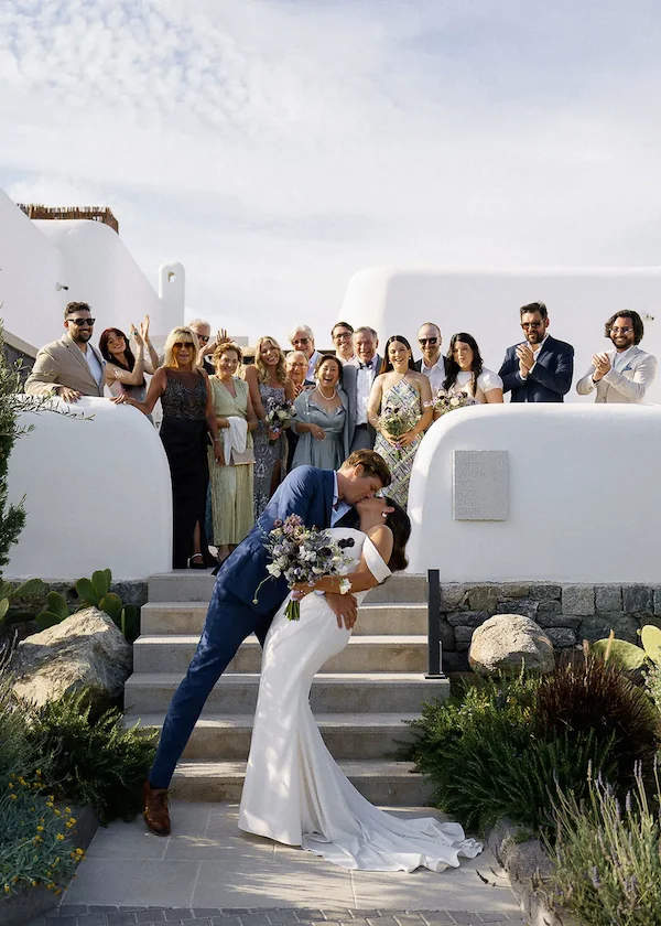 groom kisses bride while guests look on at kalesma mykonos