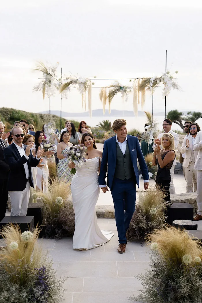 bride and groom newlyweds holding hands while guests look on at a wedding in greece at kalesma mykonos