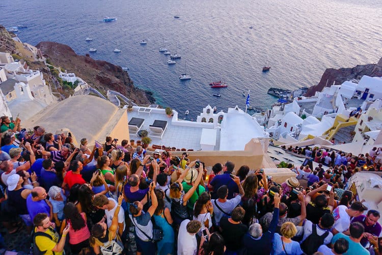 tourists pack a cliffside in santorini to take pictures of the caldera views