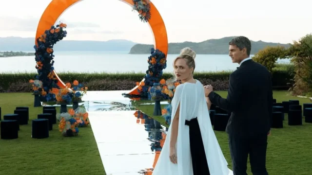 bride and groom walk down the aisle with a wedding arch and aegean sea view in the background
