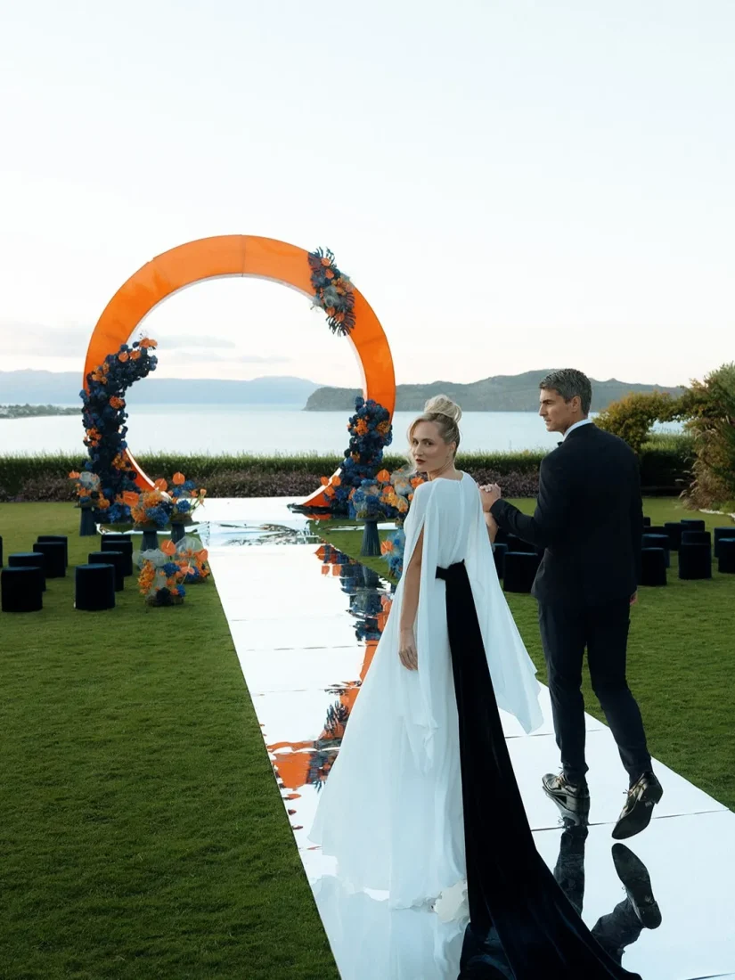 bride and groom walk down the aisle with a wedding arch and aegean sea view in the background
