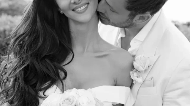 a groom kissing his new bride both wearing white in a black and white photo