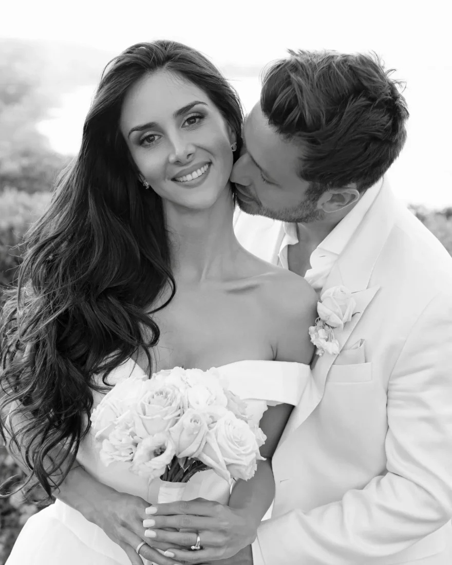 a groom kissing his new bride both wearing white in a black and white photo