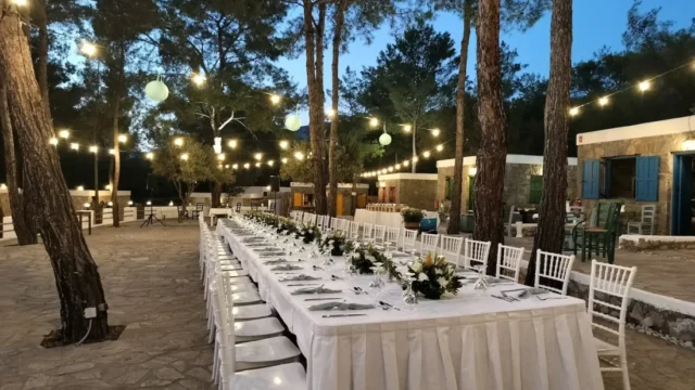 Banquet tables under festoon lights in the pine forest at Kaminari Village, Rhodes