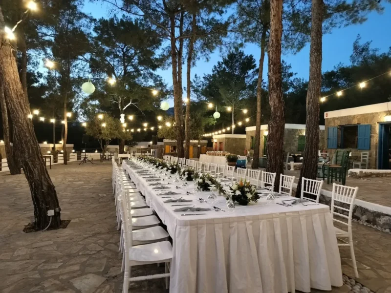 Banquet tables under festoon lights in the pine forest at Kaminari Village, Rhodes