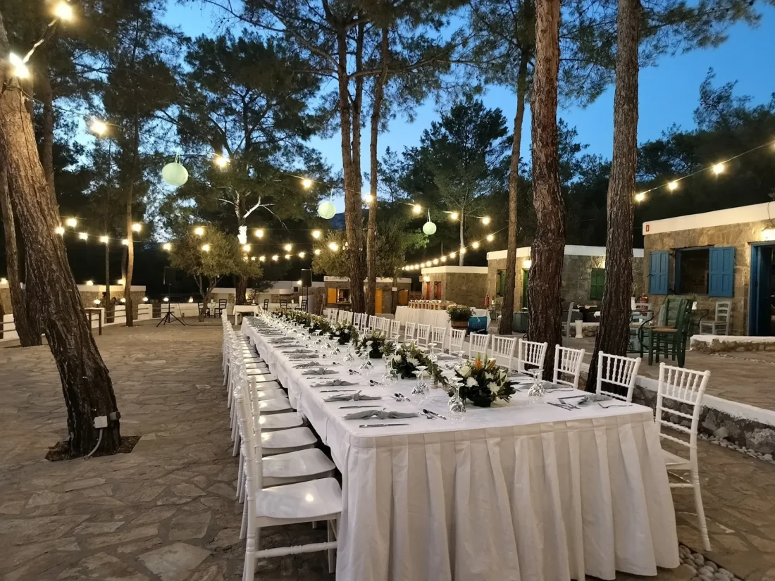 Banquet tables under festoon lights in the pine forest at Kaminari Village, Rhodes