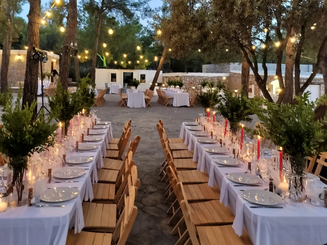 Long banquet table lit by candles under the pines at Kaminari Village, Rhodes