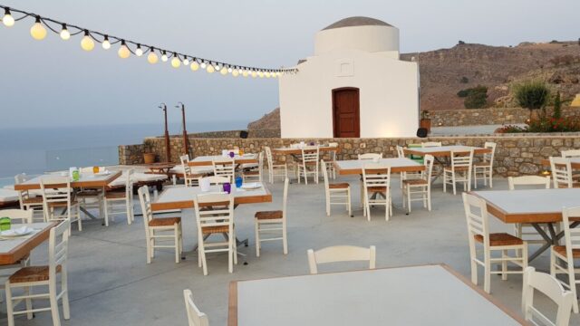 Dining tables under festoon lights on the terrace at Ktima Lindos, with the chapel behind