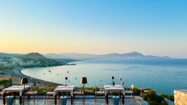 Dining tables along the terrace edge at sunset overlooking Vlicha bay at Ktima Lindos
