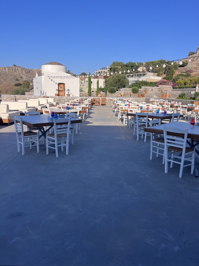 Tables set out on the terrace with the chapel and Lindos beyond at Ktima Lindos