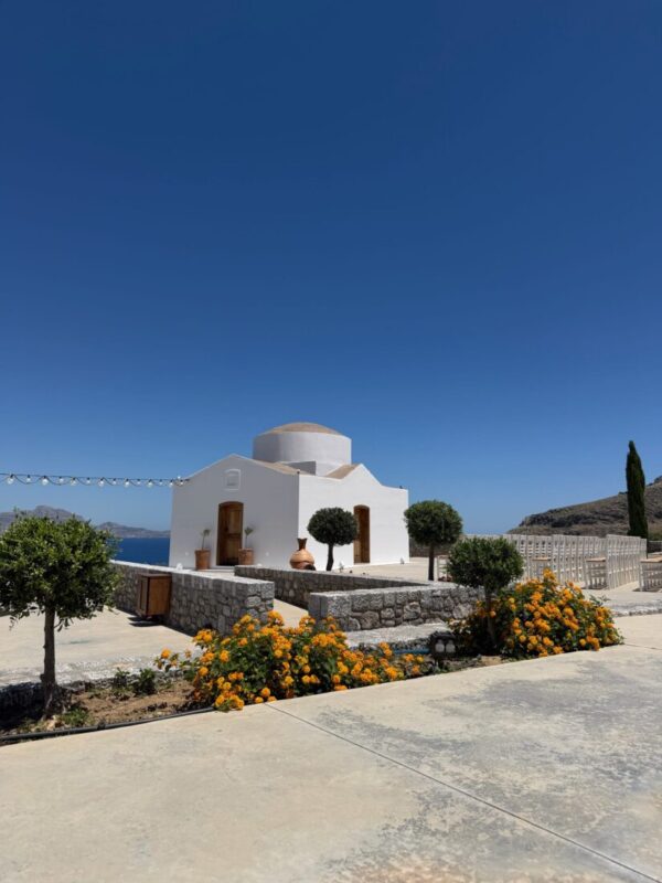 The whitewashed chapel with an olive tree and flowering shrubs at Ktima Lindos