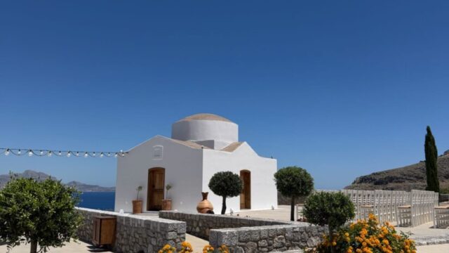 The whitewashed chapel with an olive tree and flowering shrubs at Ktima Lindos