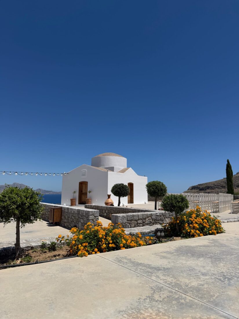 The whitewashed chapel with an olive tree and flowering shrubs at Ktima Lindos