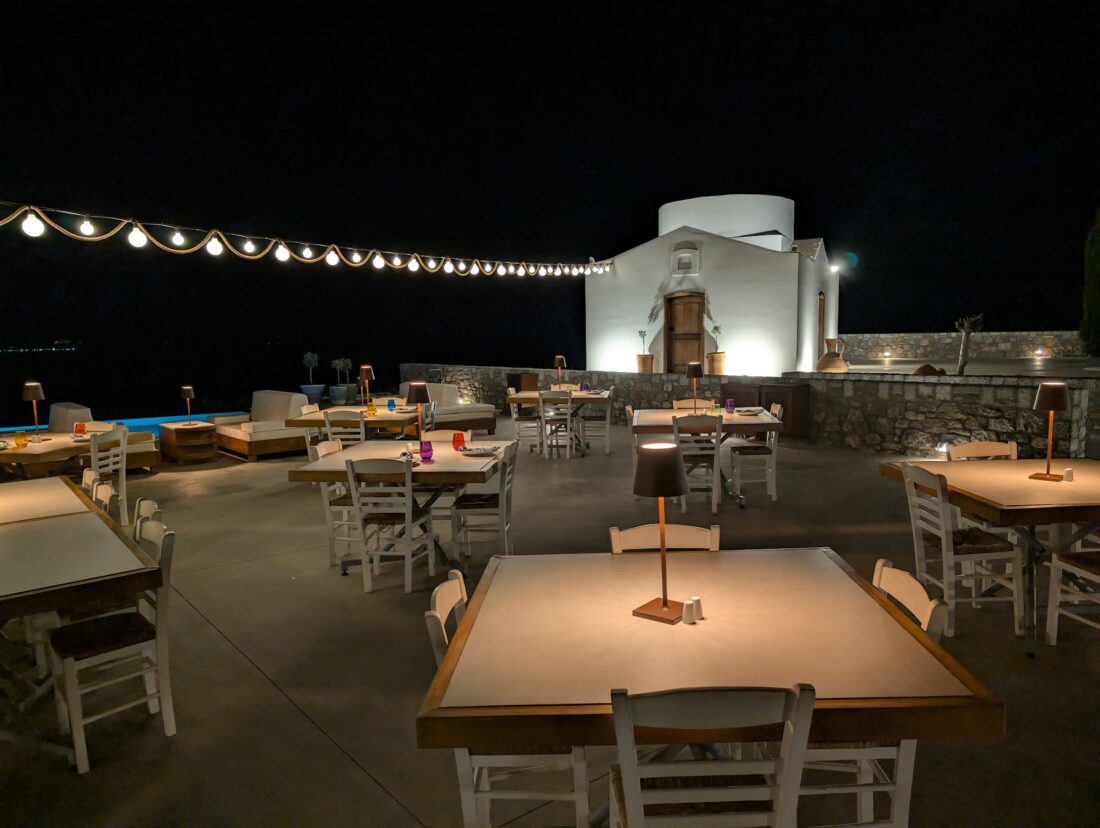 Dining tables lit at night with the chapel floodlit behind at Ktima Lindos