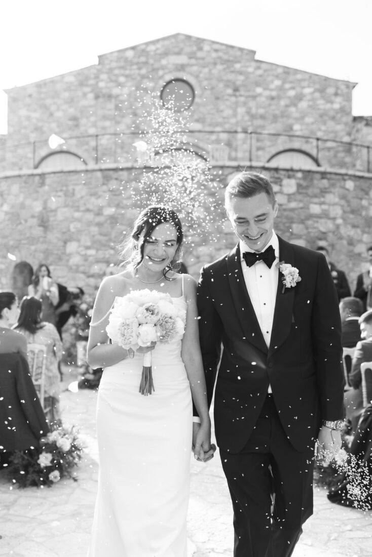 Black and white photo of Garanfil and Roman laughing under confetti after their ceremony at Pyrgos Petreza
