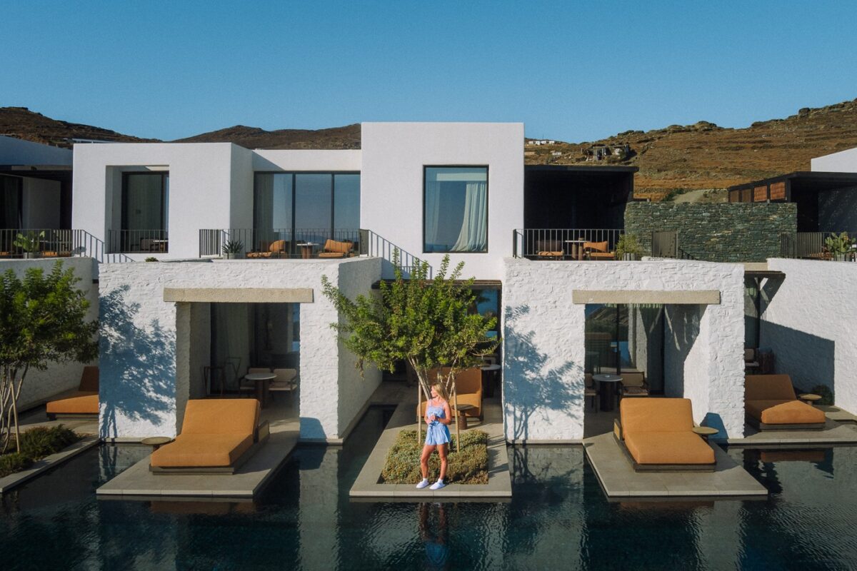Odera hotel on Tinos: white cube buildings above a long dark pool with orange loungers and dry hills behind