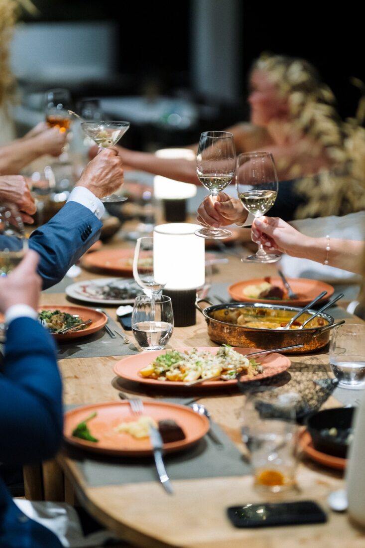 Family-style wedding dinner at a long wooden table with shared dishes and glasses raised in a toast
