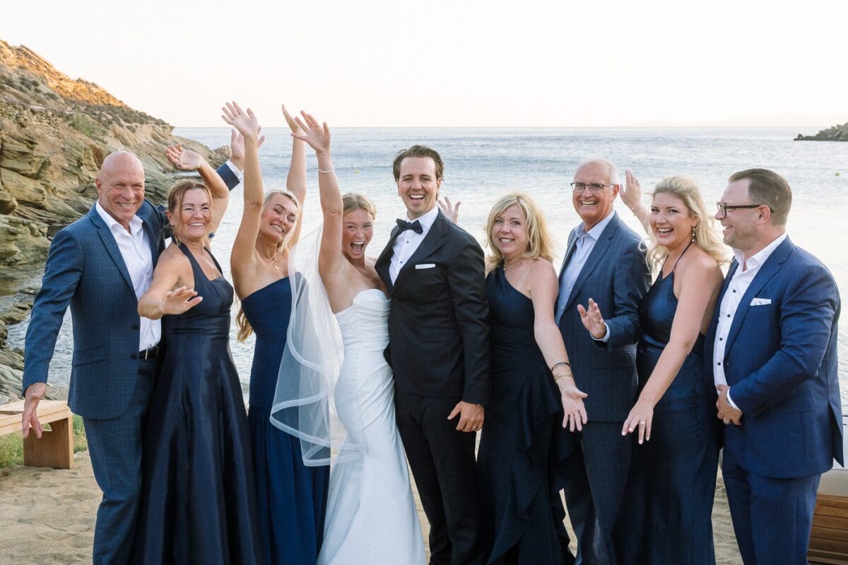 Haley and Mitch with their seven family members on the beach, arms raised and laughing, the sea behind them